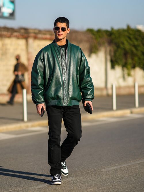 Street Style Look von der Milan Fashion Week, wo ein Gast eine grüne Bomberjacke aus Leder, mit schwarzer Denim, schwarzer Sonnenbrille und Nike Sneaker trägt.