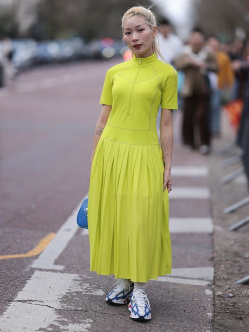 Street Style Look von der Paris Fashion Week, wo ein Gast ein neongrünes Kleid, blauer Tasche und Performance Sneaker trägt.