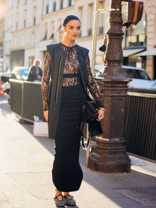 woman wearing black lace shirt, black pants in street, neo-goth trend