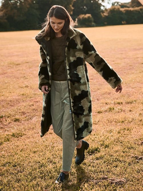 Frau mit grüner Hose und Mantel geht über ein Feld.