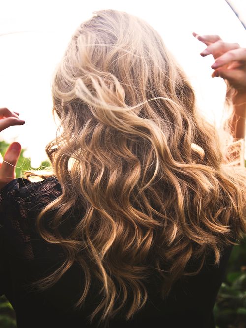 Blonde Frau mit langen lockigen Haaren, die ihre Hände in die Luft hält.