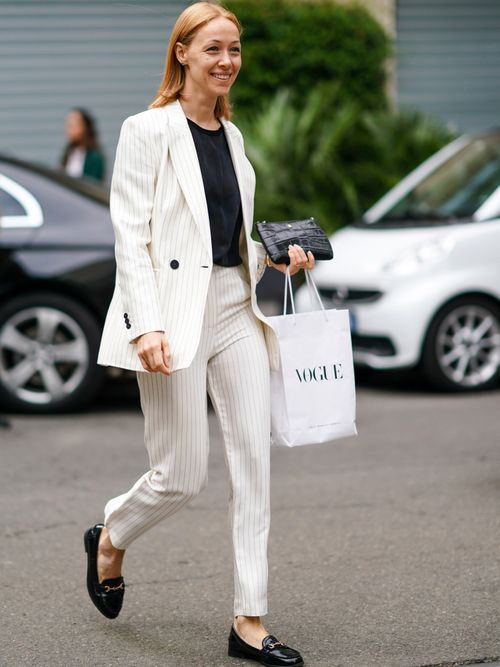 Milan Fashion Week Street Style Look von einem Gast der einen Hosenanzug in Nadesltreif mit schwarzem T-Shirt und schwarzen Loafer trägt.