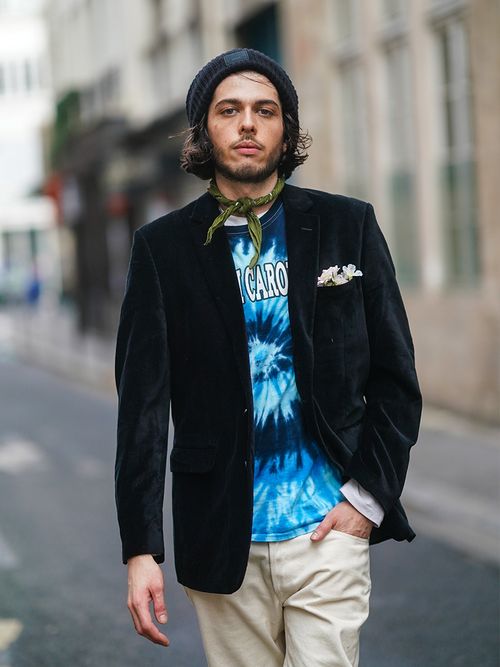 Close-up von einem Mann mit Acne Beanie, einem Batik-Shirt, einem dunkeln Sakko und einem grünen Halstuch.