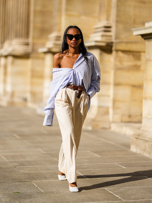 Emilie Joseph trägt eine hellblaue Bluse, beige Bundfaltenhose mit Gürtel und Sonnenbrille in Paris.