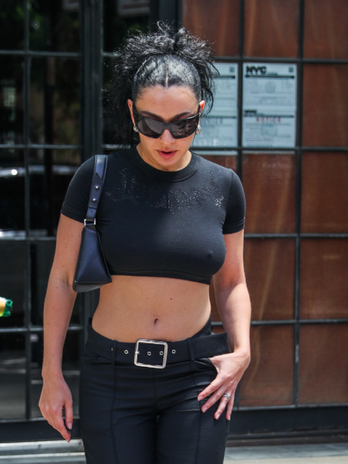Charli XCX wears a pair of oversized sunglasses with a cropped black t-shirt and jeans