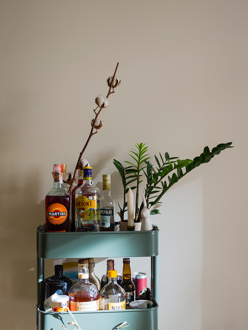 Ein türkiser Servierwagen mit vielen alkoholischen Flaschen, einer Pflanze und einer Kerze.