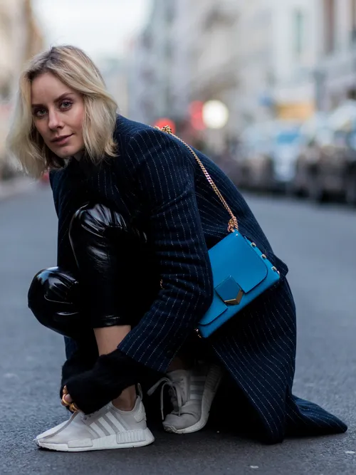 Influencerin Lisa Hahnbueck trägt einen Mantel in Nadelstreif und Lederhose. Sie bindet sich gerade die Schuhe zu.