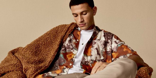 Mann mit einem gemusterten Hemd und einer braunen Decke auf der Schulter.