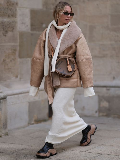Street Style Look von Karin Teigl aka constantlyk trägt ein weißes Strickkleid mit beiger Jacke, Schal, Boots und Sonnenbrille in Wien.