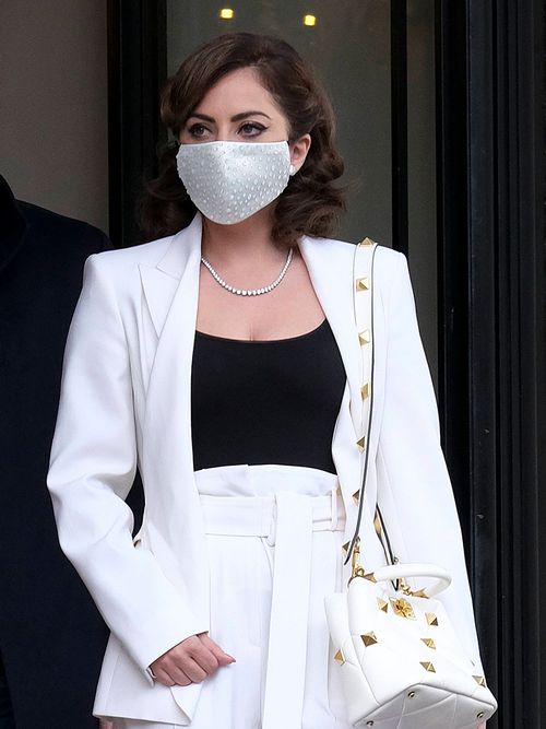 Lady Gaga mit einer Gesichtsmaske und einem weißen Hosenanzug.