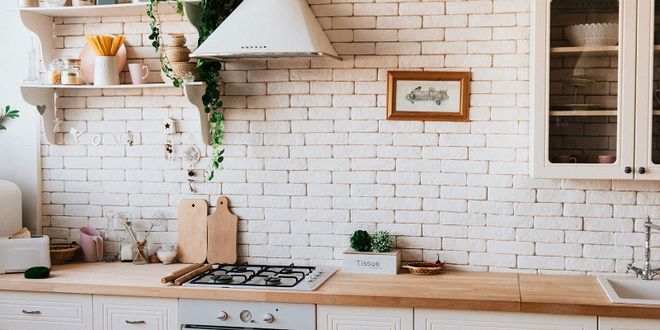 Weiße Küchenzeile mit holzfarbener Arbeitsplatte einem Gasherd und zwei offenen Wandregalen.