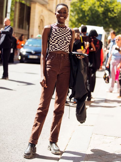 A guest wears a checkered print brown and white sleeveless top, matching brown straight leg jeans, and black boots.