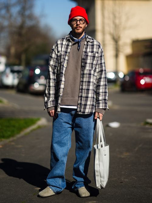 Street Style Look von der Milan Fashion Week, wo ein Gast ein kariertes Flanellhemd, mit braunem T-Shirt, Bandana-Halstuch, Beanie, Sonnenbrille, Baggyjeans und Birkenstock trägt.