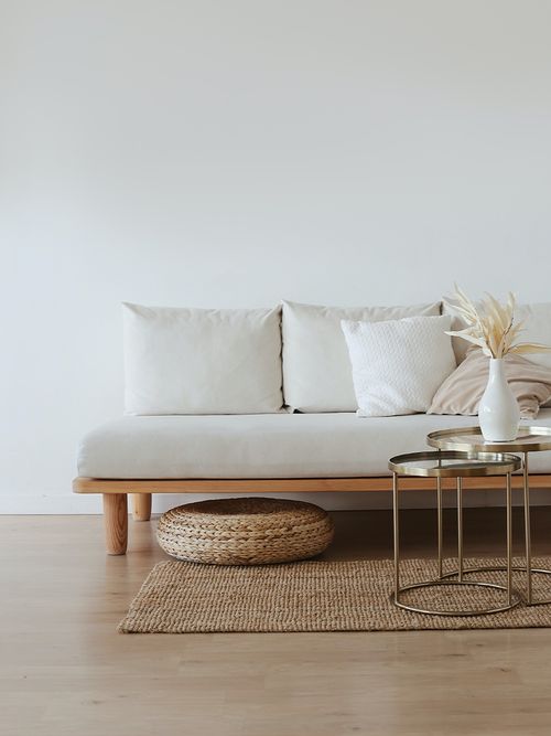 Weises Sofa auf einem Rattanteppich und Hocker.