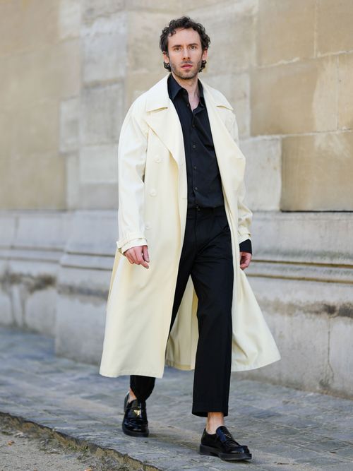 Lukas Osiecki trägt einen hellen langen Mantel, mit schwarzem Hemd und schwarzer Hose in Paris.
