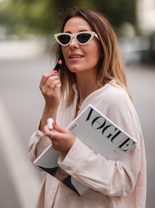 Streetstyle in blassrosa Musselinbluse und einer weißen Cateye-Brille, die sich gerade die Lippen schminkt.