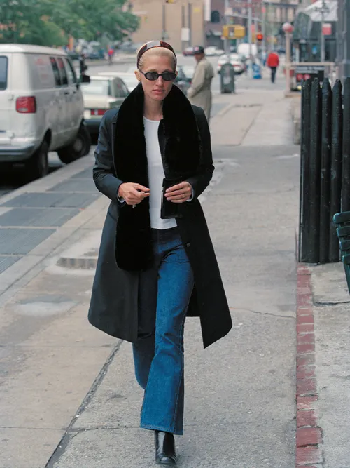 Carolyn Bessette Kennedy wears a classic long black coat, jeans, and black boots