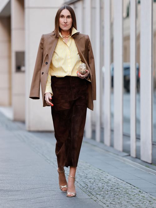 Netti Weber trägt eine gelb gestreifte Bluse mit einem braunen Bleistiftrock und beigen Blazer über die Schultern in Berlin.