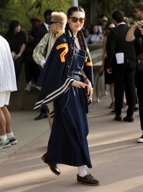 Street Style Look von der Paris Fashion Week, wo ein Gast ein Denim Outfit mit Collegejacke und Bootsschuhen trägt.