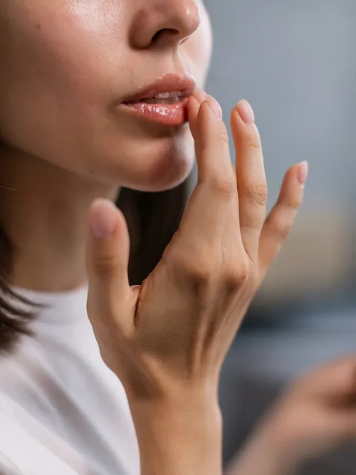 Frau in weißem T-Shirt, die sich auf die Lippen greift.