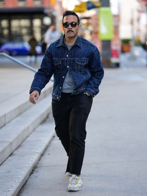 Ein Gast auf der New York Fashion Week trägt eine Jeansjacke darunter ein graues T-Shirt mit schwarzer Hose und Sonnenbrille.
