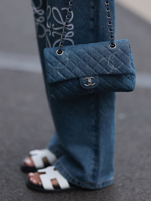 Close-up von weißen Hermes Sandalen, einer weiten Jeans und einer Chanel Tasche.