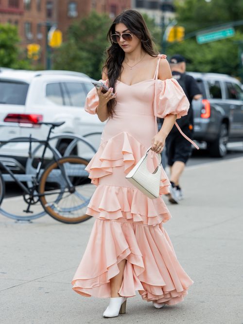 Street Style von der New York Fashion Week, wo ein Gast ein rosafarbenes Kleid mit Carmen Ausschnitt und weißen Schuhen sowie weißer Handtasche trägt.