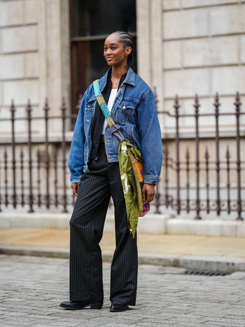Street Style Look von der London Fashion Week, wo ein Model eine oversized Denimjacke mit einer Nadelstreifhose und Umhängetasche trägt.