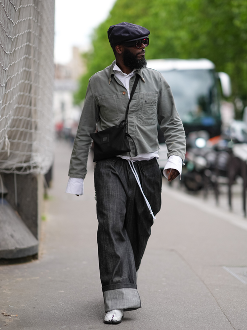 Street Style Look von der Paris Fashion Week, wo ein Gast eine graue Jacke, weißes Hemd, Crossbody-Bag, dunkelblaue Denim mit weißen Tibi Stiefel trägt.