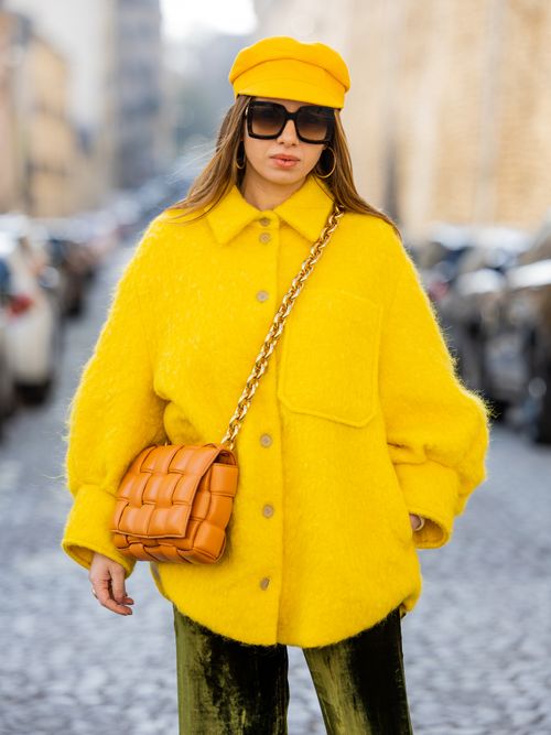 Maria Rosaria Rizzo trägt eine gelbe Jacke und passenden gelben Hut mit orangefarbener Tasche und grüner Hose auf der Milan Fashion Week.