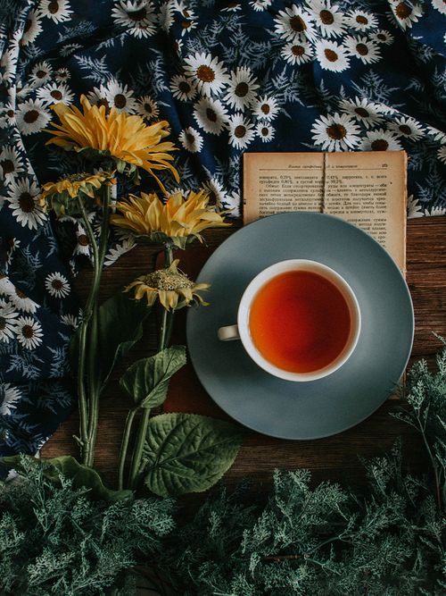 Eine Tasse mit schwarzem Tee, die auf einem Buch steht und gertocknete Blumen liegen daneben.