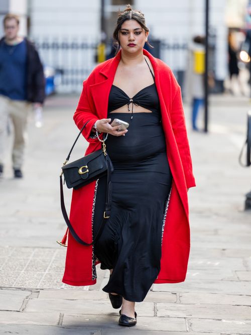 Street Style Look von der London Fashion Week, wo ein Gast einen roten Mantel mit schwarzem Kleid und einer Coach Tasche trägt.