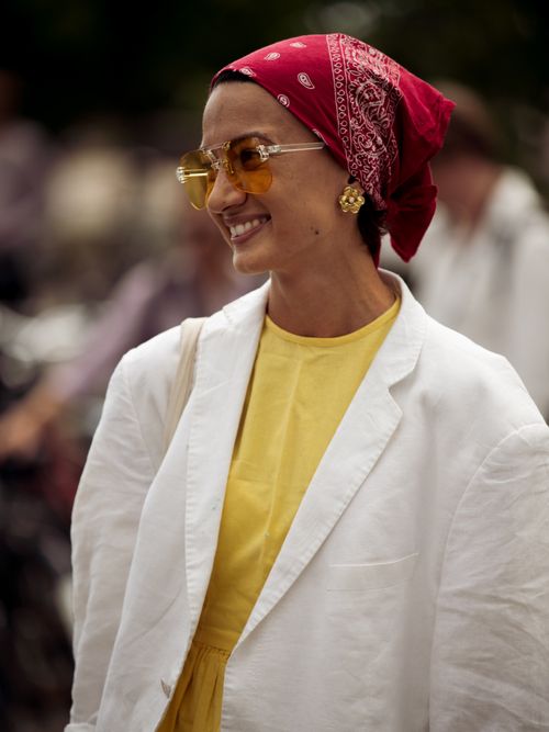Street Style Look von der Copenhagen Fashion Week, wo ein Gast ein rotes Bandana als Kopftuch, mit einer gelben Brille, weißen Blazer und gelben Top darunter, trägt.