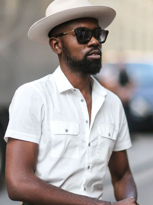 Street Style Look von der Paris Fashion Week, wo ein Gast ein weißes kurzärmliges Hemd trägt, mit Hut und Sonnenbrille.