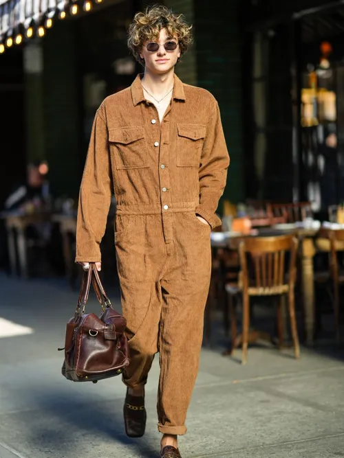 A guest wears brown coveralls with a leather bag and loafers