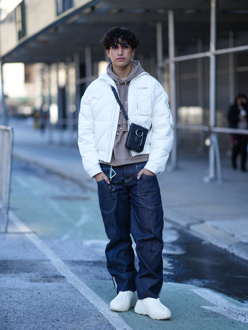 Street Style Look von einem Gast der eine weiße Daunenjacke trägt im Bomber Schnitt mit Hoodie und Denimhose