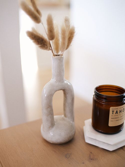 Moderne Vase mit Trockenblumen steht neben einer braunen Duftkerze.