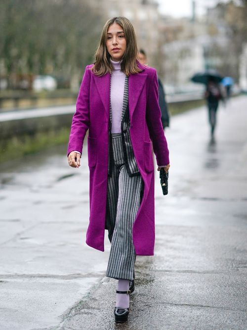 Street Style Look von der Paris Fashion Week. Lilafarbener Mantel mit rosa Rollkragen, gestreifter Hose und Plateau Schuhe mit Strümpfen.