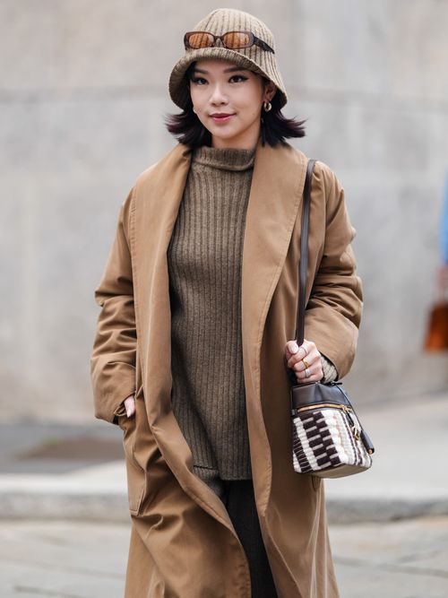 Willabelle Ong wears light brown hat, dark brown sunglasses, on head, silver earrings, dark brown sweater, dark brown sweater pants, light brown suede shoes, light brown coat, dark brown and white leather bag, outside Sportmax, during the Milan Fashion Week Spring/Summer 2024-2025 on September 20, 2024 in Milan, Italy.