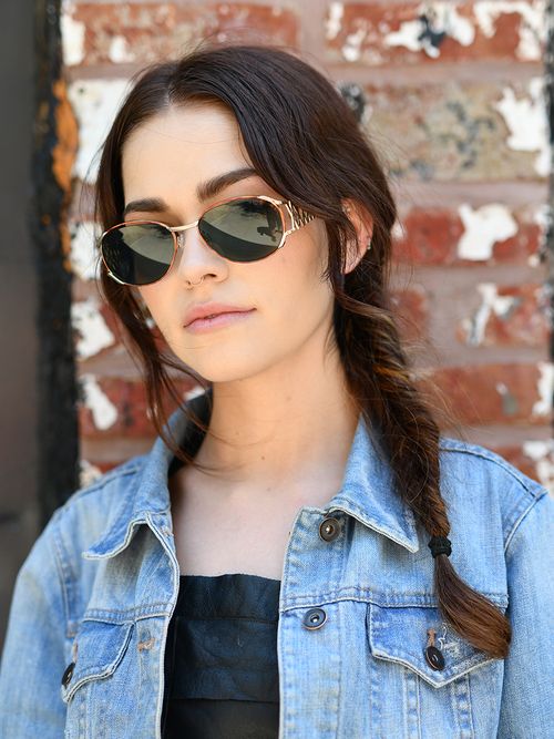 Frau mit Jeansjacke, Sonnenbrille und einem Fischgrätenzopf.