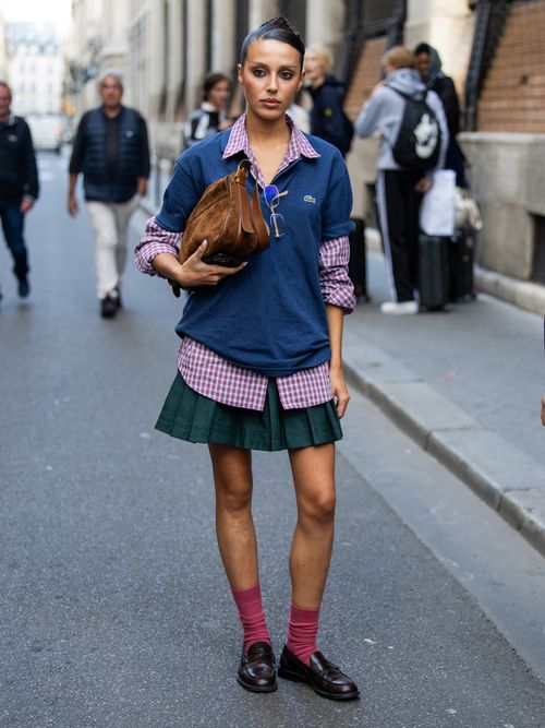 Marina Suarez trägt einen Lacoste-Pulli, darunter ein Karohemd, Faltenrock, Socken und Loafer auf der Paris Fashion Week.