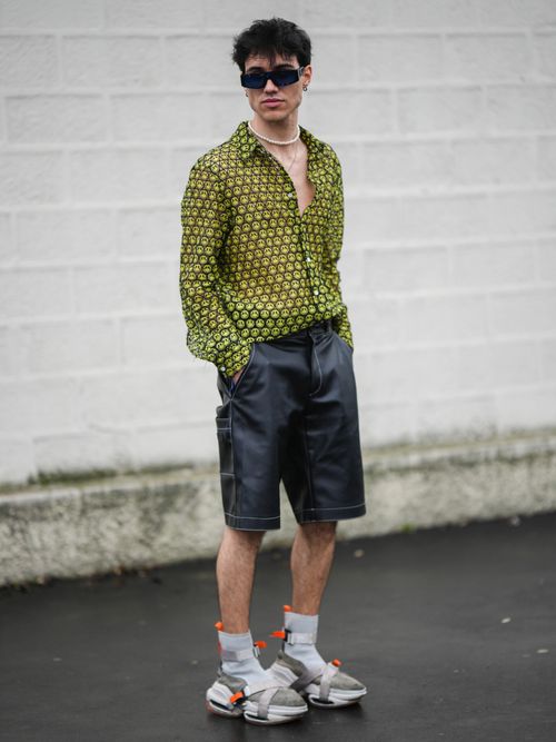 Street Style Look von der Milan Fashion Week, wo ein Gast ein grün gemustertes Hemd, eine Leder Cargoshorts mit Sonnenbrille und Perlenkette trägt.