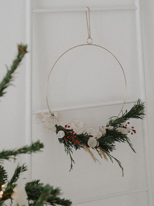 Metallkranz der an einer weißen Leiter hängt und zum Teil mit Trockenblumen geschmückt ist.
