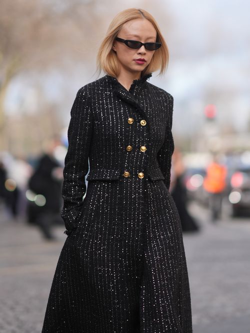 iki Wu Jie wears sunglasses, red lipstick, a black double breasted tweed long coat with golden buttons and glittering shiny details, outside Giambattista Valli, during the Womenswear Fall/Winter 2024/2025 as part of Paris Fashion Week on March 01, 2024 in Paris, France.