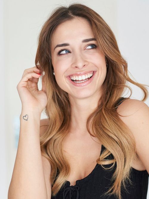 Lächelnde Frau mit einem Herz Tattoo am Arm.