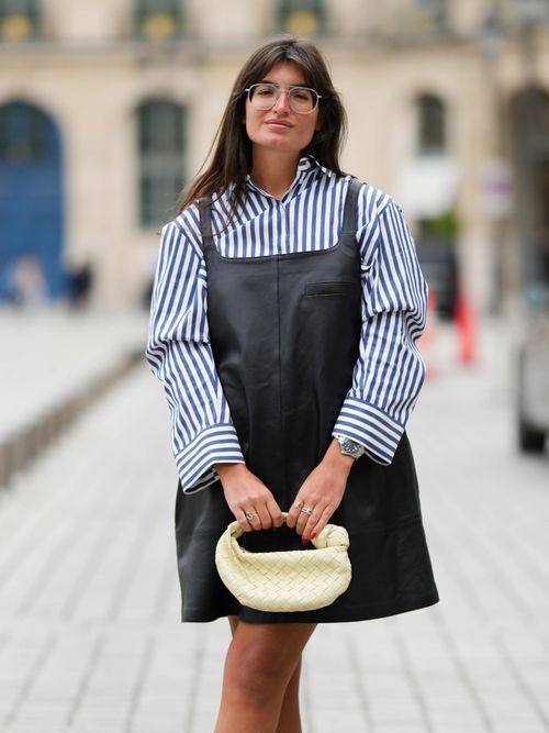 Street Style Look aus Paris, wo ein Gast ein Lederkleid mit gestreifter Bluse darunter und weißer Tasche trägt.