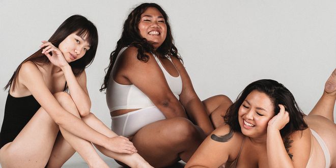 Drei Frauen in Unterwäsche die auf dem Boden sitzen und liegen und lachen.