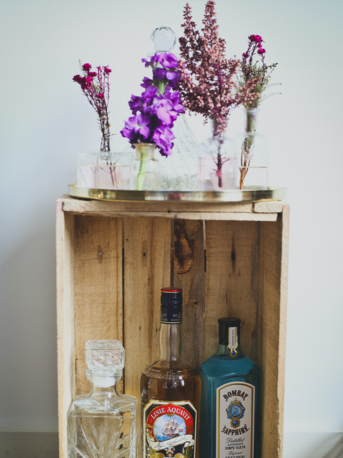 Eine Holzkiste gefüllt mit alkoholischen Getränken und darauf ein Tablett mit Blumen.