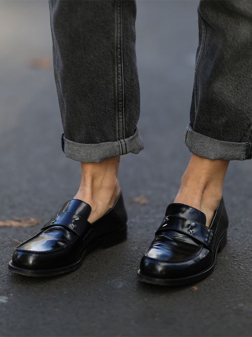 Close up von Beinen in einer grauen Jeans, die umgekrempelt wurde und dazu schwarze Loafers.