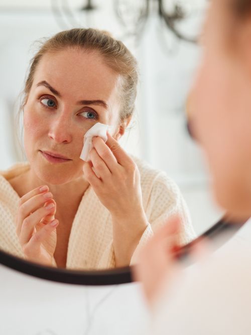 Frau, die sich im Spiegel gerade ihren Mascara runterwischt.